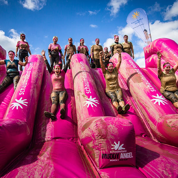 Teilnehmer des Schlammlaufes Muddy Angel Run rutschen auf eine aublasbare Rutsche runter